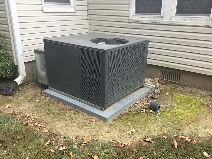 Packaged HVAC unit on a concrete pad beside an older sided home in the Arkansas River Valley, the kind of install online cost calculators cannot see