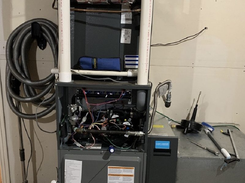 Open furnace cabinet with exposed control wiring, PVC venting, and technician tools during a River Valley replacement in an older home